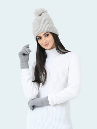 Woman wearing a gray knit hat, white sweater, and gray gloves on a light gray background