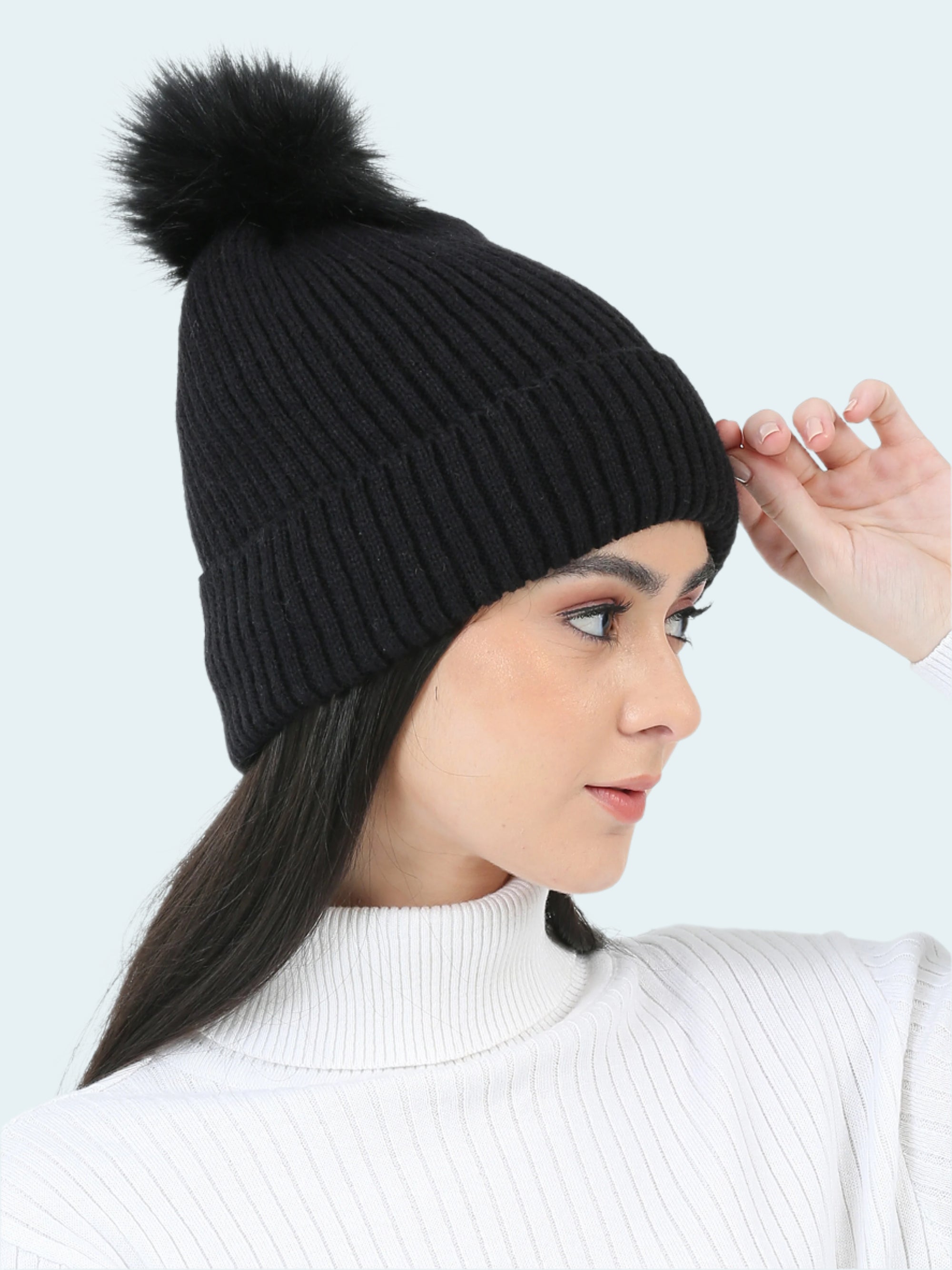Woman wearing a black knit beanie with a pom-pom on a white background