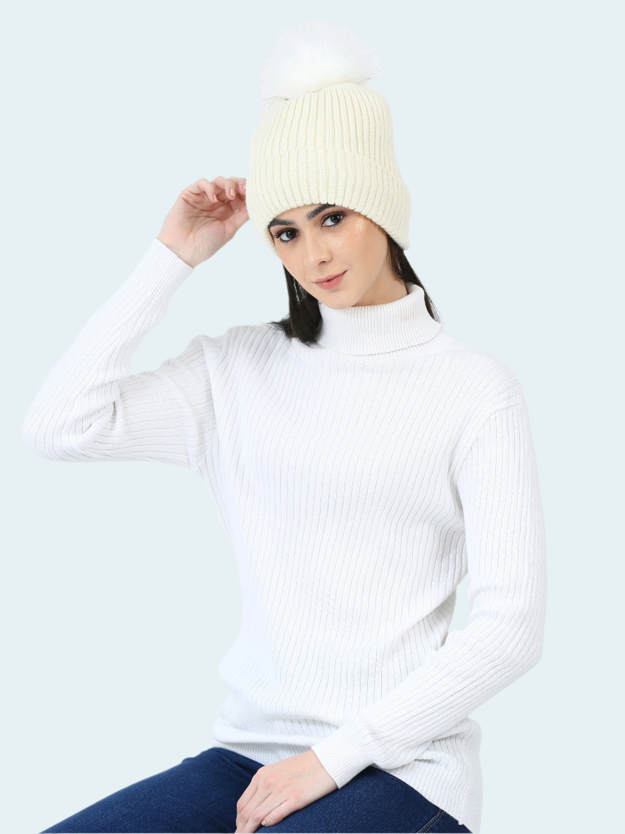 Woman wearing a white ribbed sweater and cream beanie against a white background
