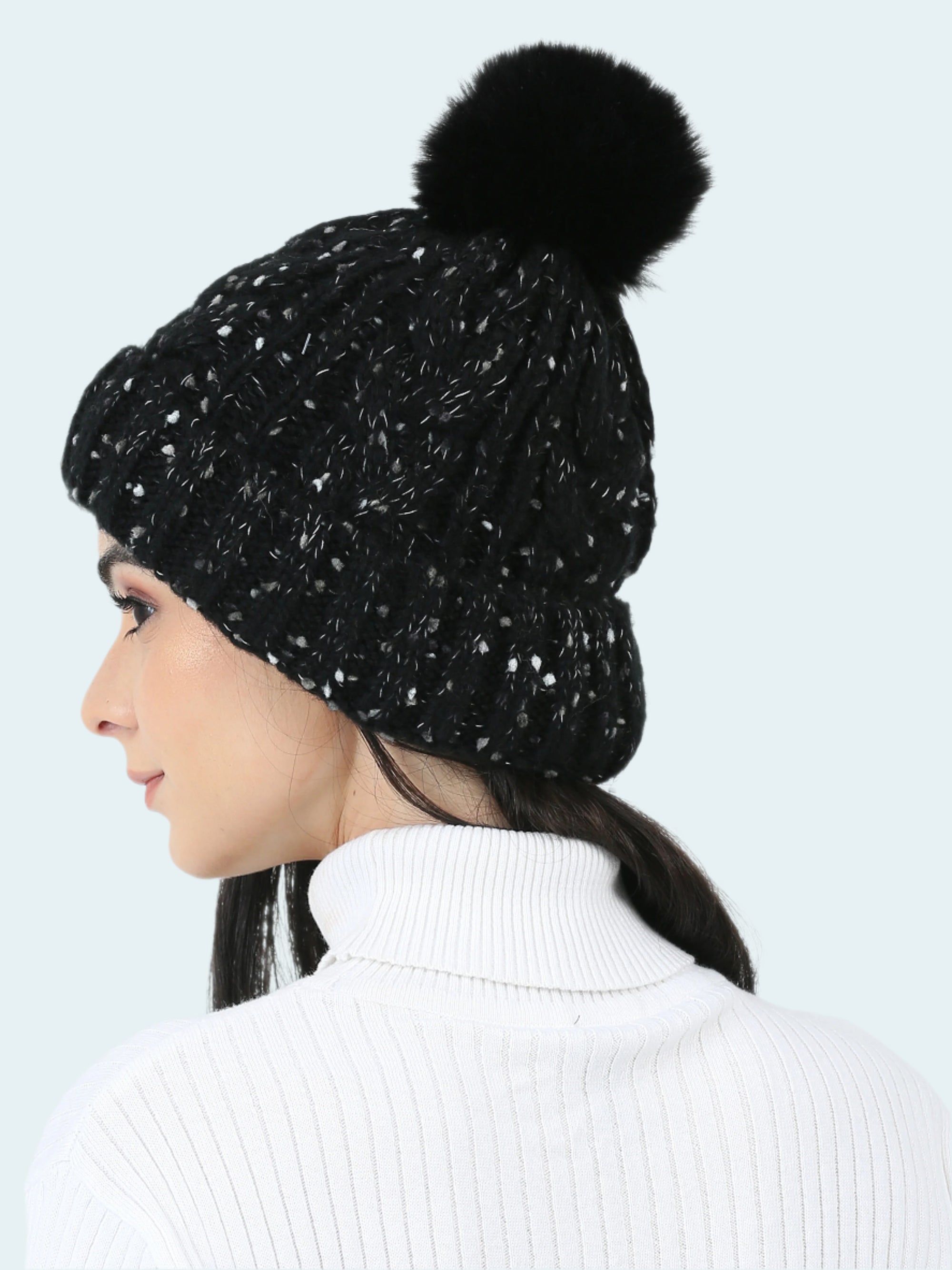 Black beanie with a pom-pom worn by a person on a white background