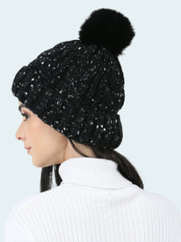 Black beanie with a pom-pom worn by a person on a white background