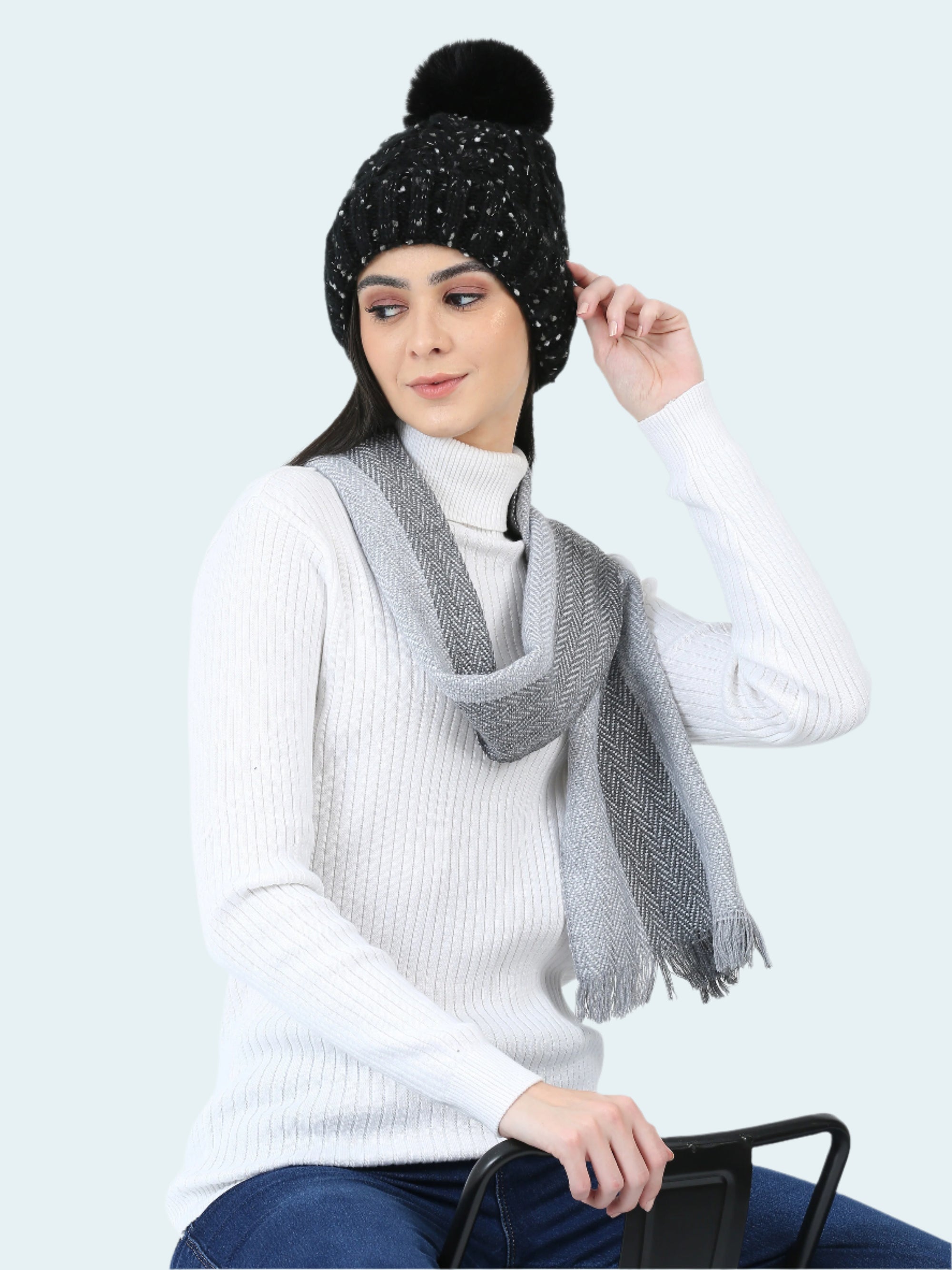 Woman wearing a black beanie with a pom-pom and a gray scarf on a white background