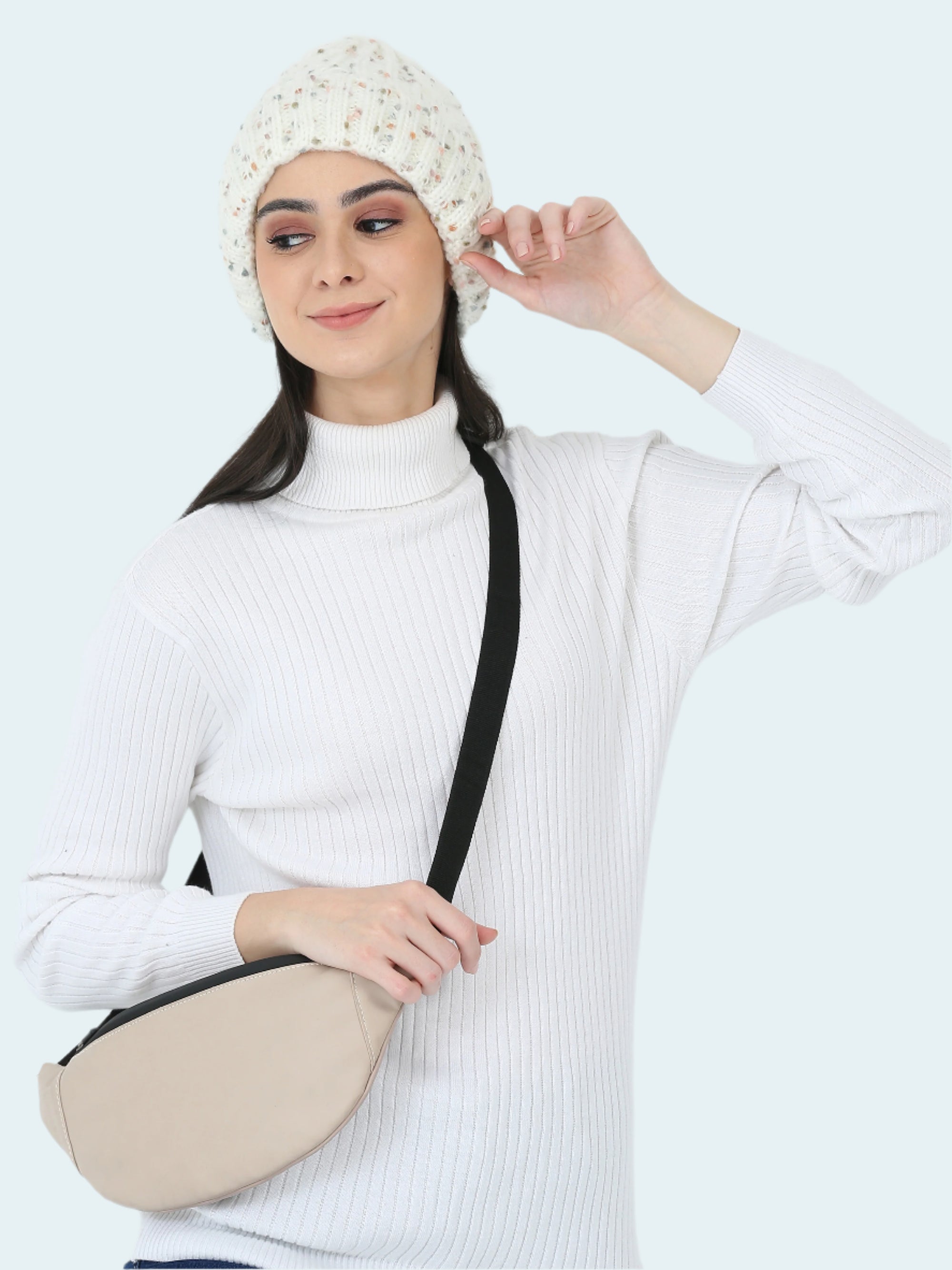 Woman wearing a white beanie and holding a beige crossbody bag against a white background