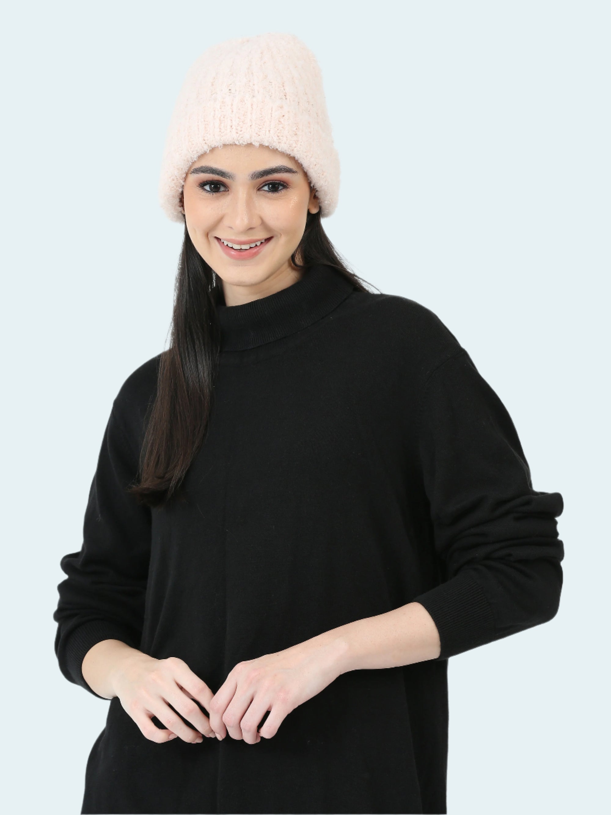 Woman wearing a black sweater and light pink beanie on a white background