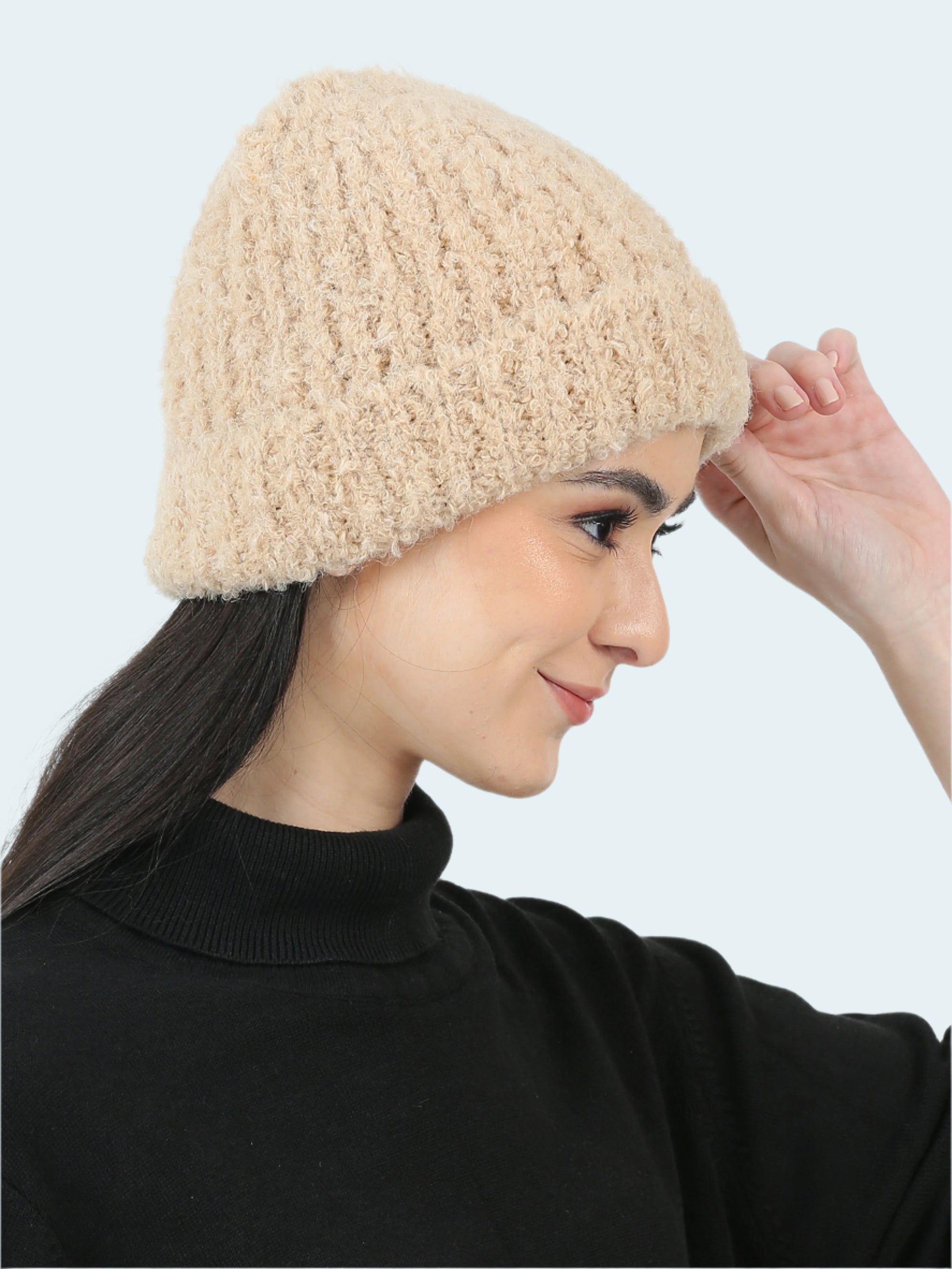 Woman wearing a beige knitted beanie against a plain background