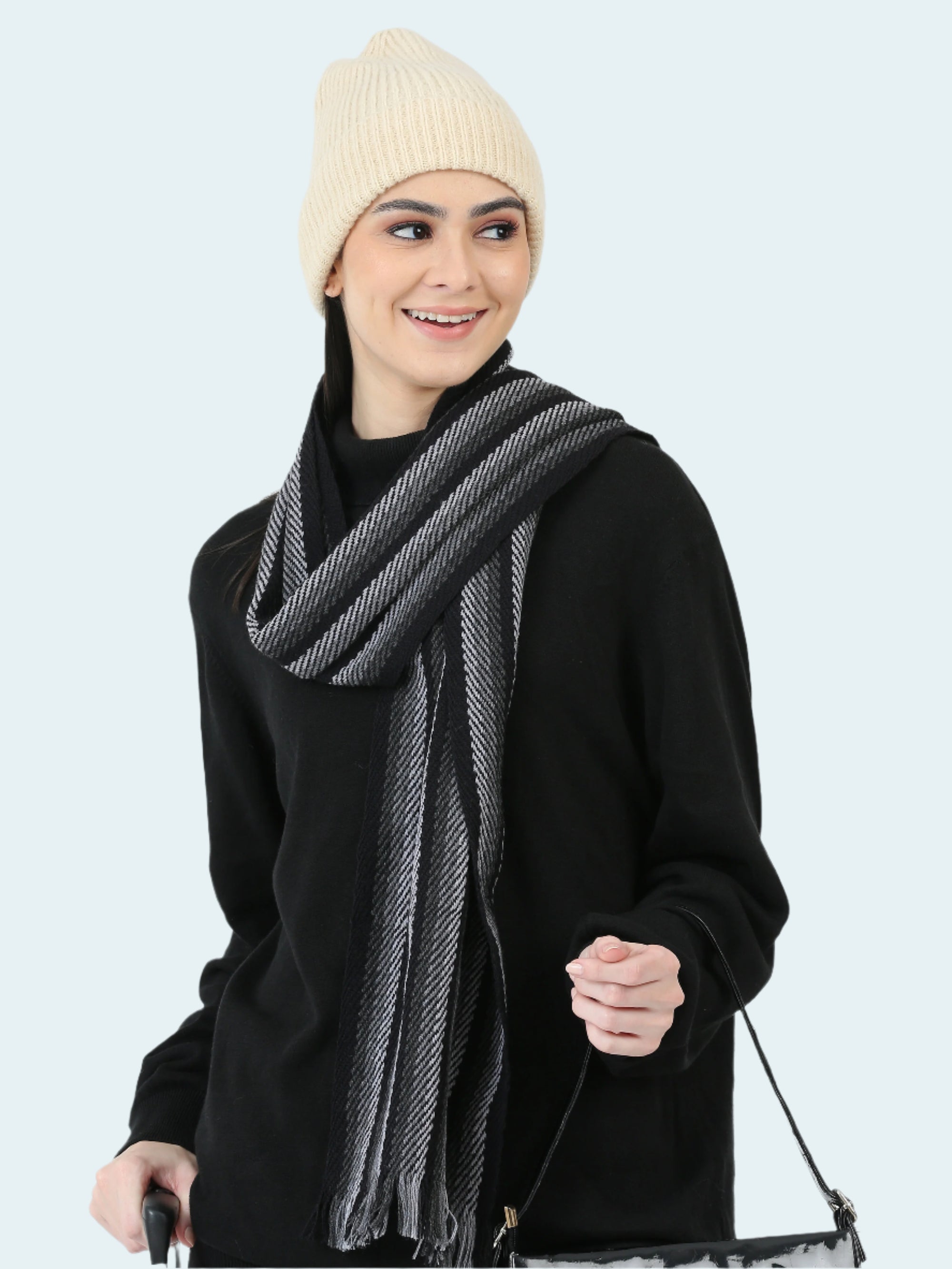 Woman wearing a black outfit with a gray scarf and cream beanie on a white background