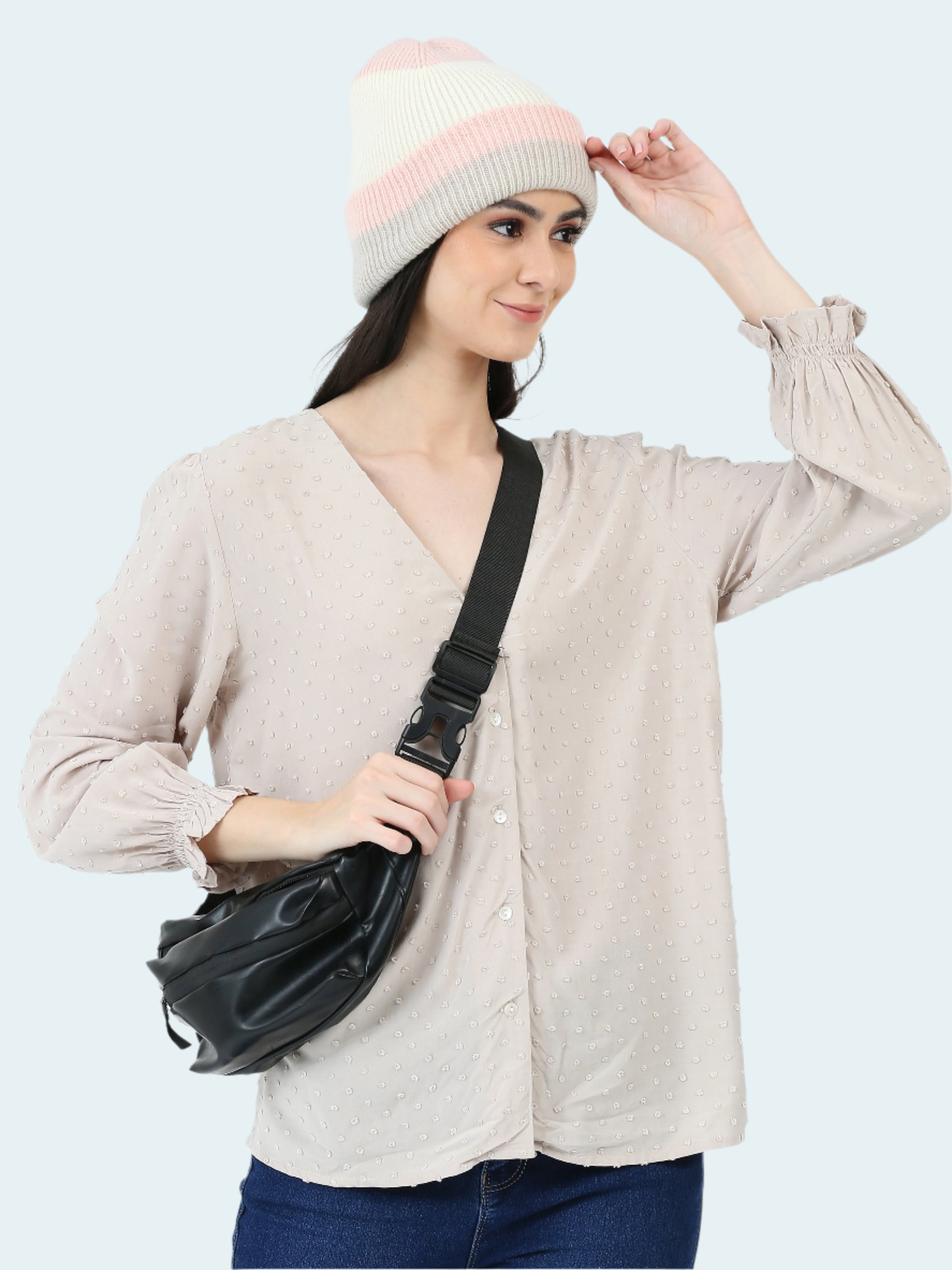 Woman wearing a beige sweater, pink and white beanie, and holding a black bag on a white background