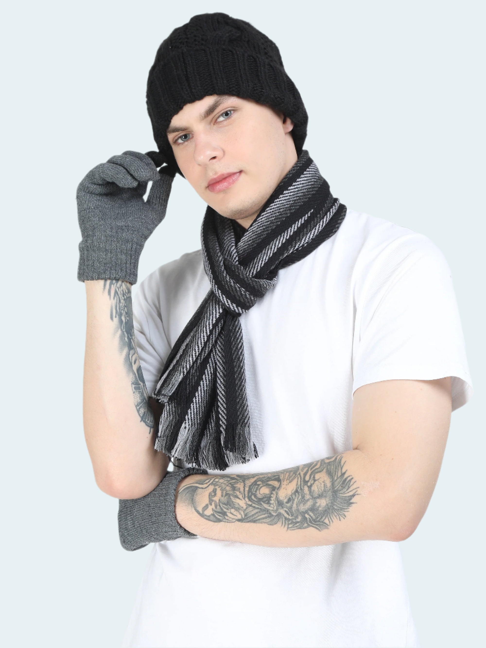 Person wearing a black knit beanie, gray gloves, and a black and gray scarf on a white background