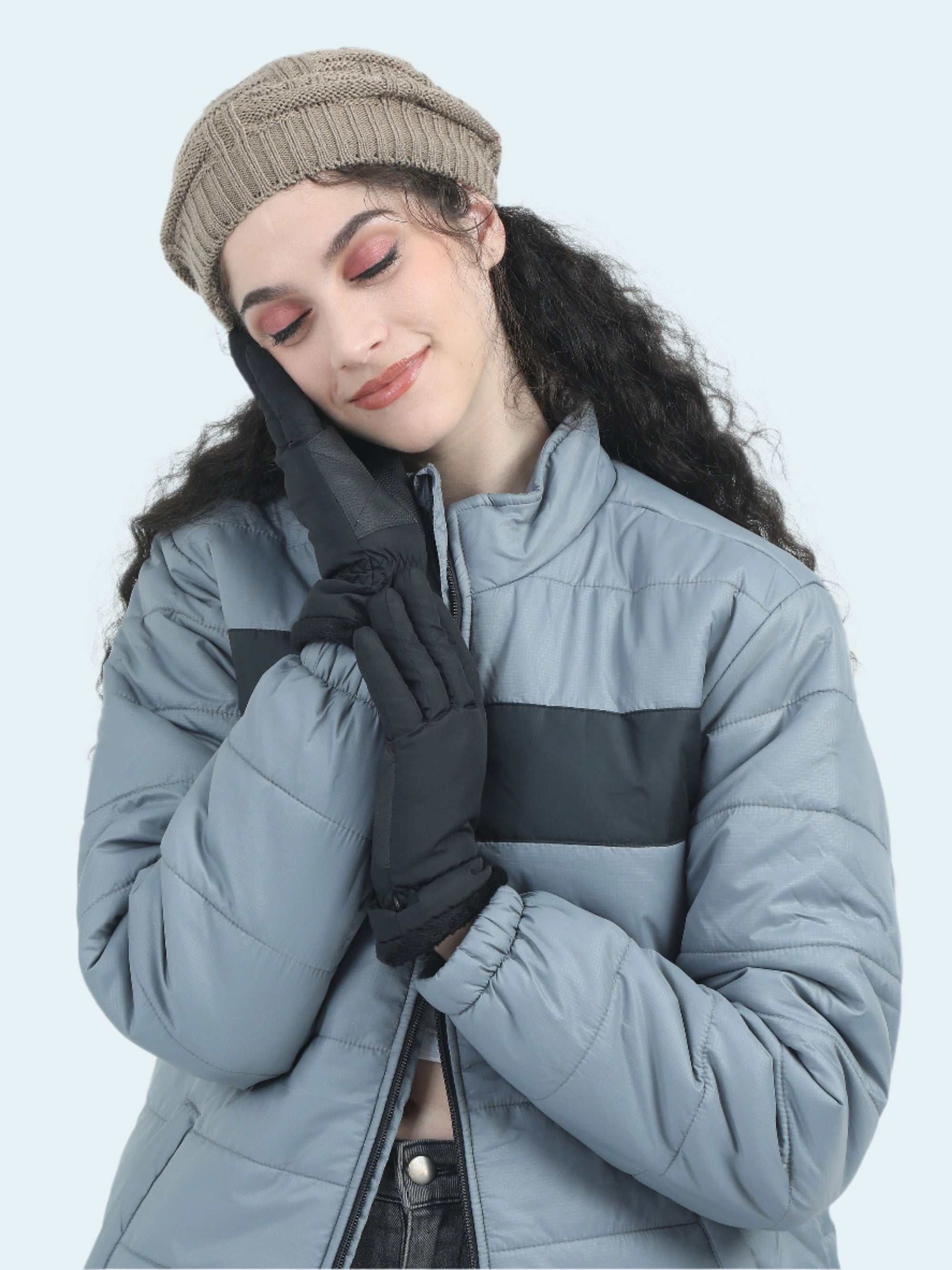 Woman wearing a gray and black winter coat with gloves and a beanie on a light gray background