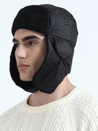Person wearing a black trapper hat with ear flaps on a light gray background