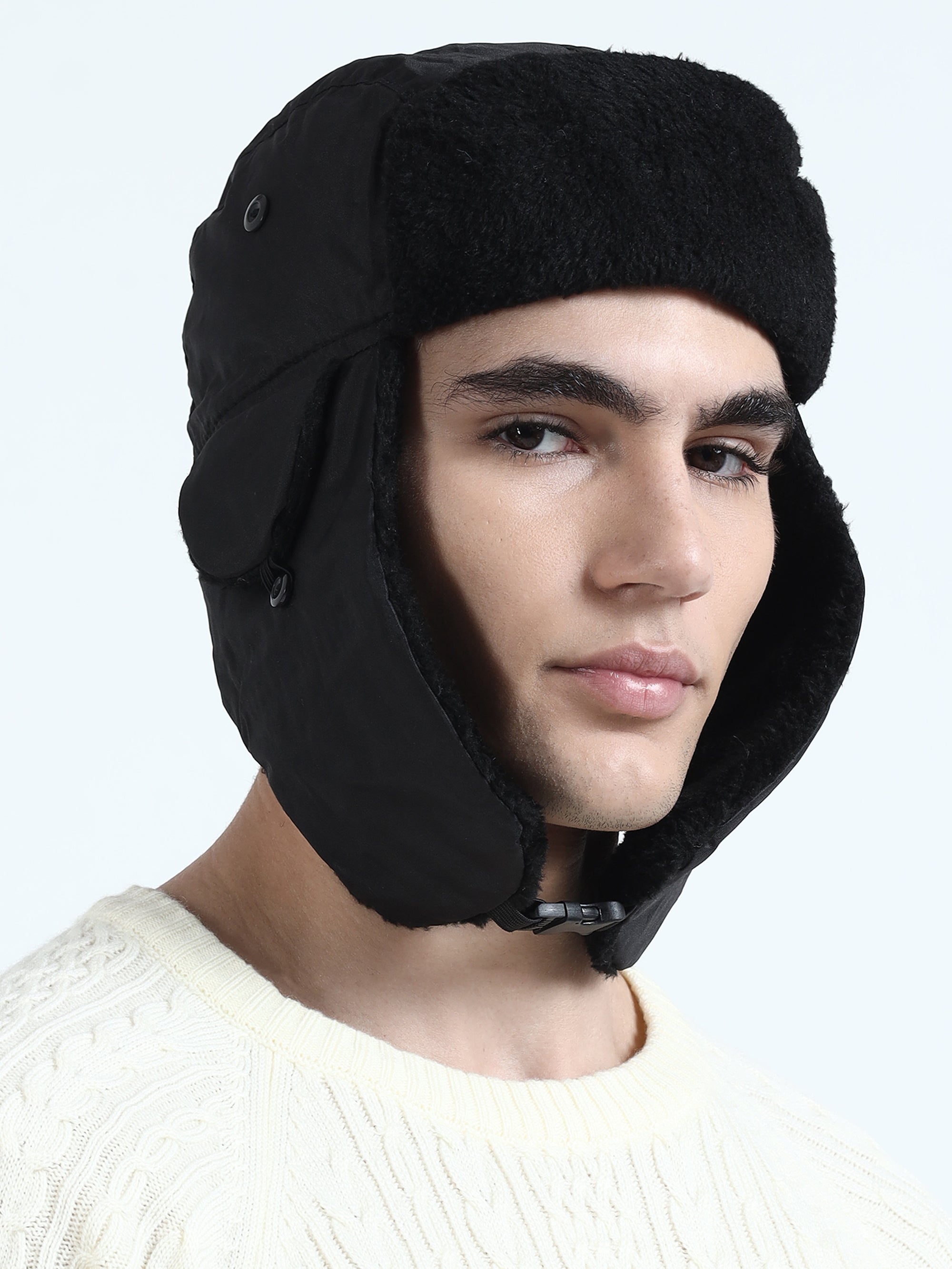 Person wearing a black trapper hat with ear flaps on a light gray background