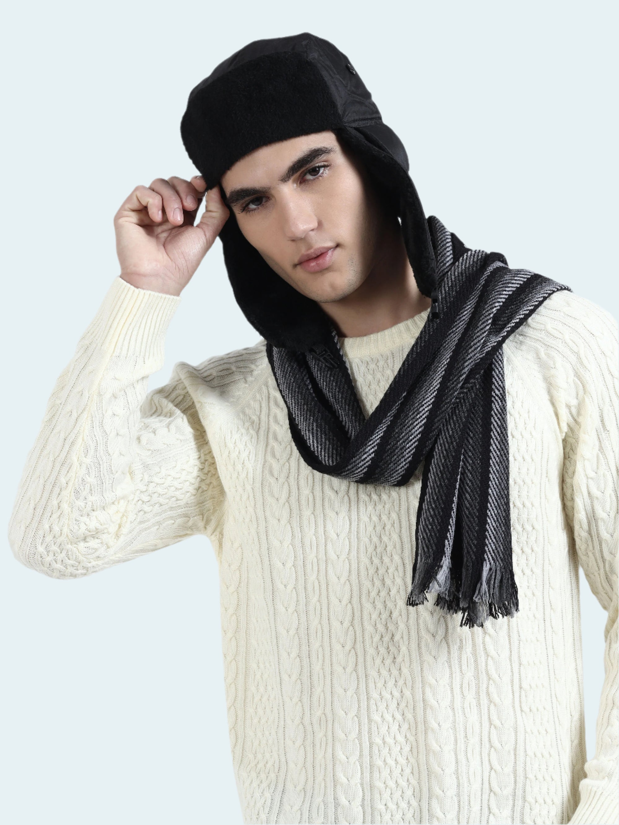 Man wearing a black beanie and scarf with a white sweater on a light gray background