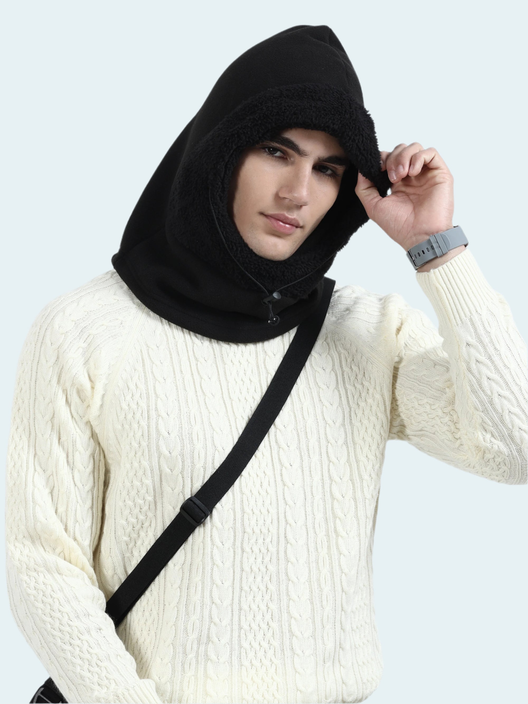 Person wearing a black hooded garment over a white sweater against a light gray background