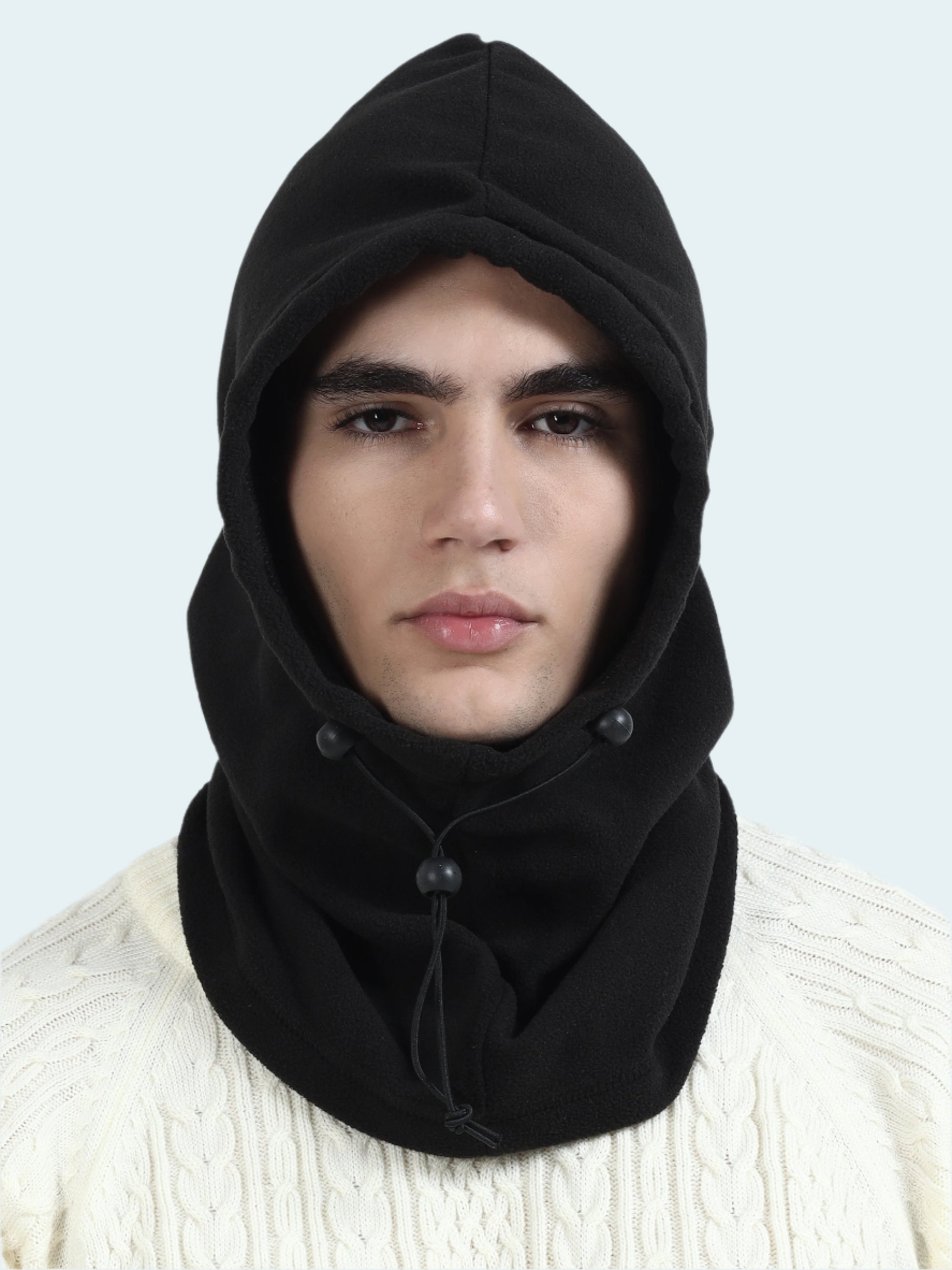 Person wearing a black hooded balaclava over a white sweater on a light gray background
