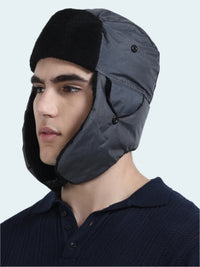 Person wearing a gray trapper  hat with black fur trim on a white background