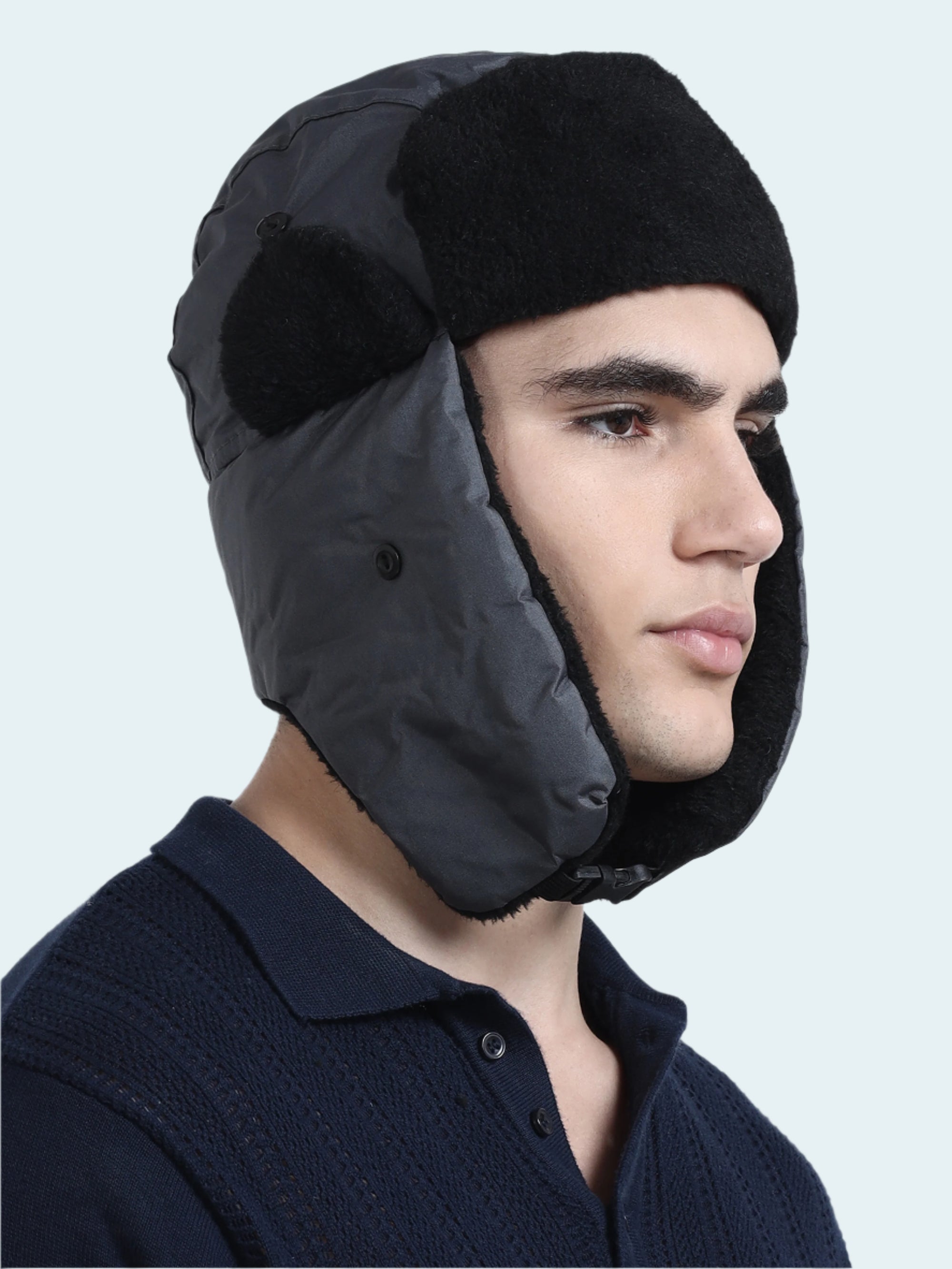Person wearing a black winter hat with ear flaps on a white background