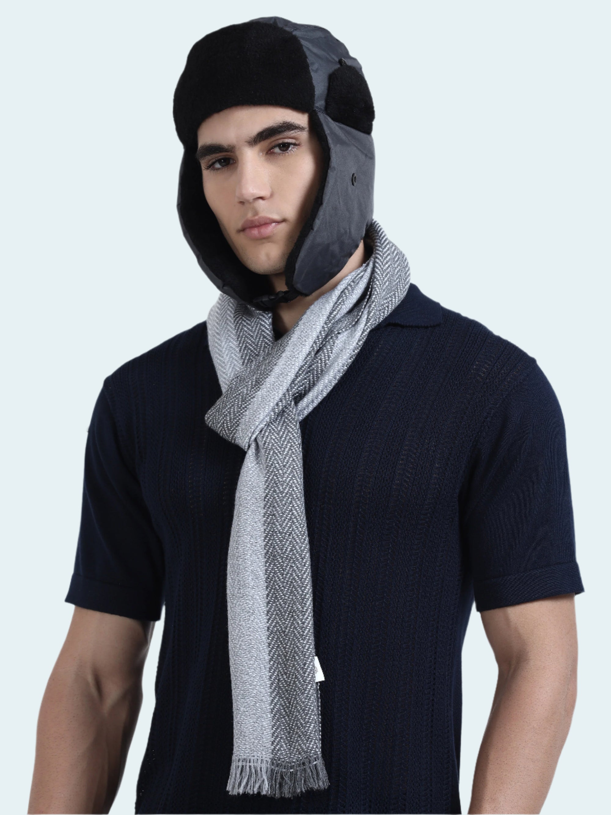 Man wearing a dark shirt and gray scarf with a black and gray trapper hat on a white background