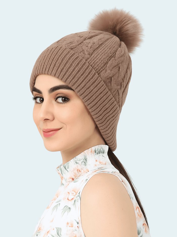Woman wearing a brown knitted beanie with a pom-pom on a light gray background