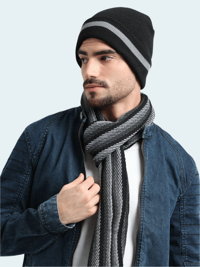 Man wearing a black beanie with a gray stripe and a striped scarf against a light gray background