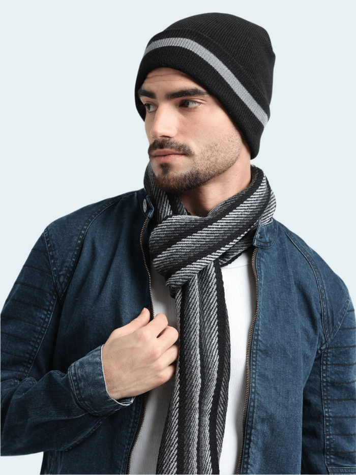 Man wearing a black beanie with a gray stripe and a striped scarf against a light gray background
